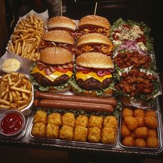 a table topped with trays of food covered in burgers and tater tots