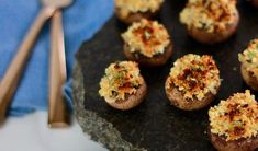 small stuffed mushrooms on a black plate with silverware and spoons next to them