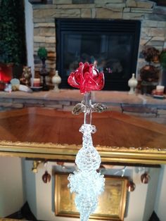 a red rose is sitting on top of a glass vase in front of a fireplace