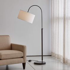 a floor lamp next to a chair in a room with white walls and drapes