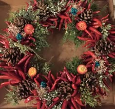 a wreath made out of red peppers and pine cones