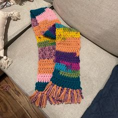 a multicolored crocheted scarf sitting on top of a couch next to a pillow