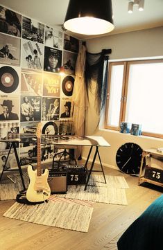 a room with a guitar, desk and various records on the wall