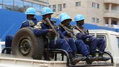 four men in blue helmets sitting on the back of a truck