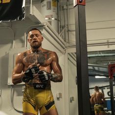 a man with tattoos on his chest standing in front of a mirror holding a pair of boxing gloves