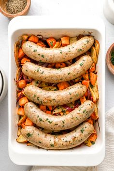 a casserole dish filled with sausages, carrots and other vegetables on a table