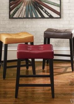 three stools in front of a brick wall and hardwood flooring with a painting on the wall behind them