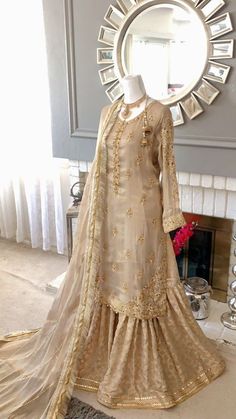 a mannequin dressed in a beige outfit with gold embroidery work on the skirt