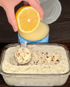 someone is squeezing an orange slice into a container with ice cream and fruit on the side