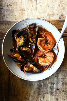 a white bowl filled with seafood and mussels on top of a wooden table