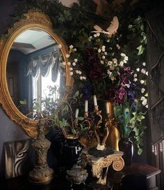 a mirror sitting on top of a table next to vases filled with flowers and birds