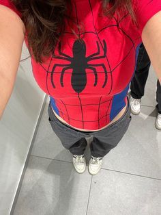 a woman wearing a red spiderman shirt is taking a selfie in the mirror