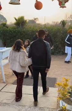 a man and woman walking down a sidewalk next to a white table with decorations hanging from it