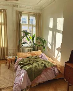 a bed sitting in a bedroom under a window next to a table with a potted plant on it