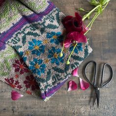 flowers and scissors are sitting on the table next to knitted cloths, which have been placed together