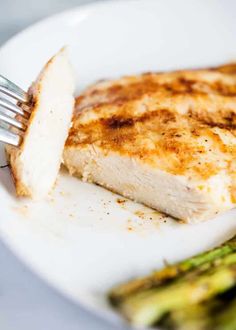 a piece of fish on a white plate with asparagus and a fork in it