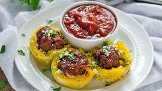 a white plate topped with stuffed peppers and meatballs next to a bowl of sauce