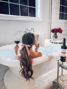 a woman sitting in a bathtub reading a book and holding a glass of wine