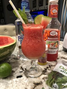 a watermelon margarita sits on a marble counter top next to bottles of gin