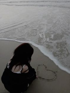 a woman sitting on top of a beach next to the ocean writing in the sand