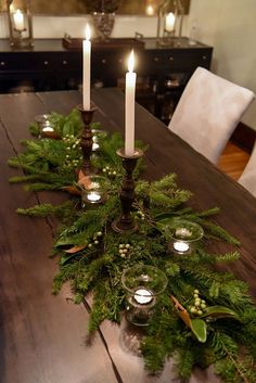 a table topped with candles and greenery on top of a wooden dining room table