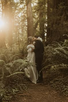 a bride and groom kissing in the woods at their wedding day with sun shining through the trees