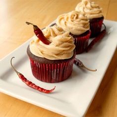 three cupcakes on a white plate topped with frosting and chili peppers next to each other