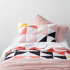 a bed topped with pillows and blankets next to a white wall