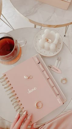 a woman's hand holding a notebook next to a cup of tea and ring binders