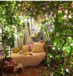 a bed covered in lots of greenery next to a wall with lights on it