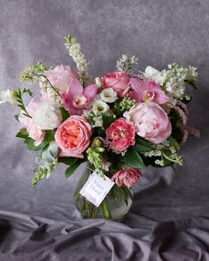 a vase filled with pink and white flowers on top of a gray cloth covered table