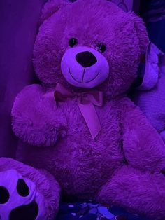 a large purple teddy bear sitting on top of a bed next to other stuffed animals