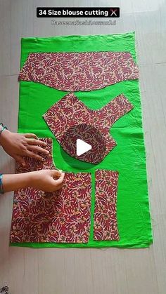 someone is making a quilt on the floor with green material and red fabric, while another person's hands are reaching for it