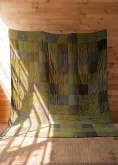 a bed with a green and brown quilt on it's side next to a wooden wall