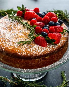 a cake covered in powdered sugar with berries and rosemary sprigs on top