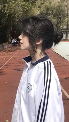 a woman with black hair wearing a white jacket and standing in front of a tennis court