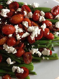 a white plate topped with asparagus and cherry tomatoes covered in feta cheese