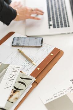 a person using a laptop computer on top of a desk next to papers and a cell phone