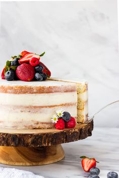 a close up of a cake on a wooden stand with strawberries and blueberries