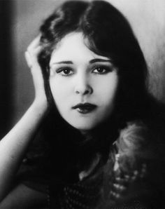 an old black and white photo of a woman with her hand on her head, looking at the camera