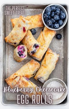 blueberry cheesecake eggrolls on a baking sheet with berries and powdered sugar