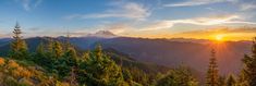 the sun is setting in the mountains with pine trees