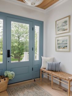 a blue front door with a bench and two pictures on the wall next to it