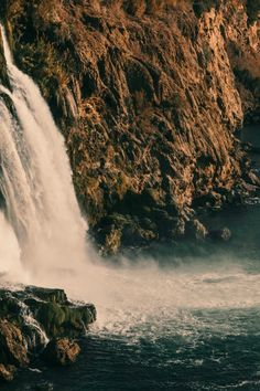 a large waterfall is coming out of the side of a cliff into the water below