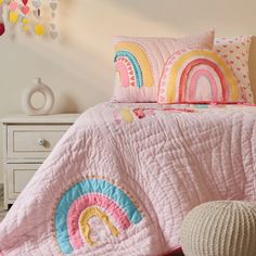 a pink bed with a rainbow quilt and pillows