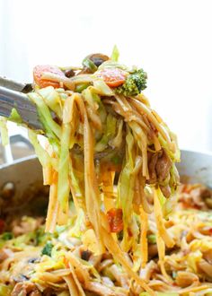 a spoon full of noodles and vegetables being lifted from a pan with broccoli