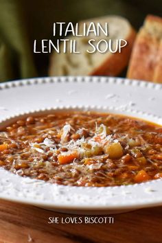 a white bowl filled with soup sitting on top of a wooden table next to bread