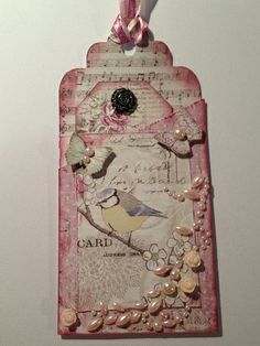 a pink tag hanging from the side of a wall with buttons and pearls on it