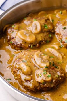 two meat patties covered in mushroom gravy in a pan on the stove