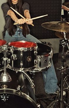 a woman with long hair sitting in front of a drum set and holding two sticks